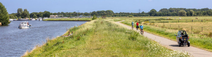 Fietsers en een scootmobieler rijden op een fietspad paralel aan rivier De Eem.