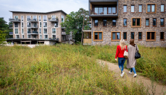 Twee vrouwen wandelen door het groen rondom lage flats