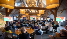 Huib van Essen en de dagvoorzitter spreken vanaf het podium de zaal met deelnemers toe