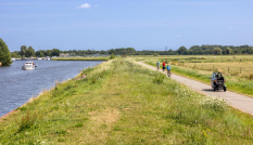 Fietsers en een scootmobieler rijden op een fietspad paralel aan rivier De Eem.
