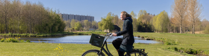 Vrouw fiets door het groen van Noorderpark-Ruigenhoek met flatgebouw op de achtergrond