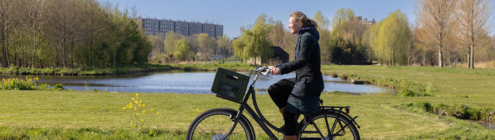 Vrouw fiets door het groen van Noorderpark-Ruigenhoek met flatgebouw op de achtergrond