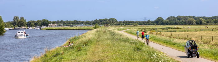 Fietsers en een scootmobieler rijden op een fietspad paralel aan rivier De Eem.