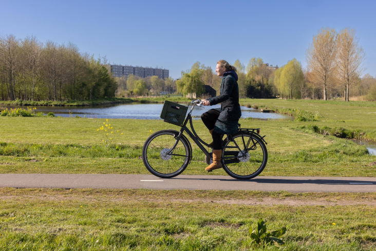 Vrouw fiets door het groen van Noorderpark-Ruigenhoek met flatgebouw op de achtergrond