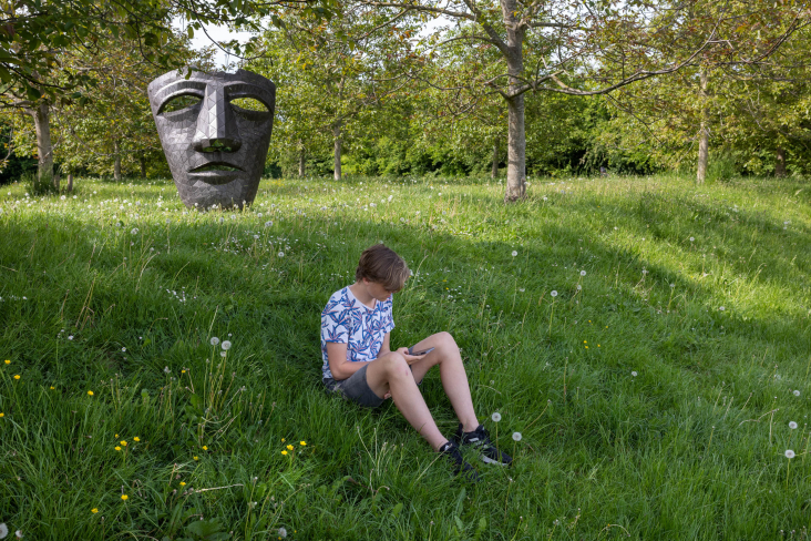 Tiener zit op zijn telefoon in het grasveld van Bos Nieuw Wulven