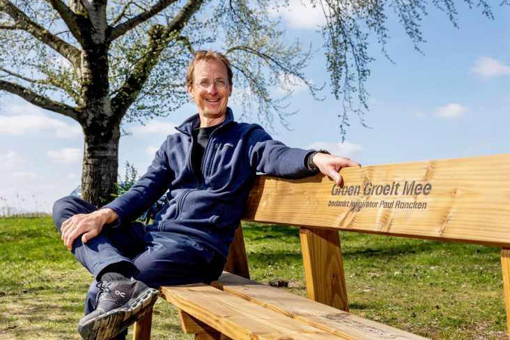 Paul Roncken zit op een bankje met het logo van Groen Groeit Mee.