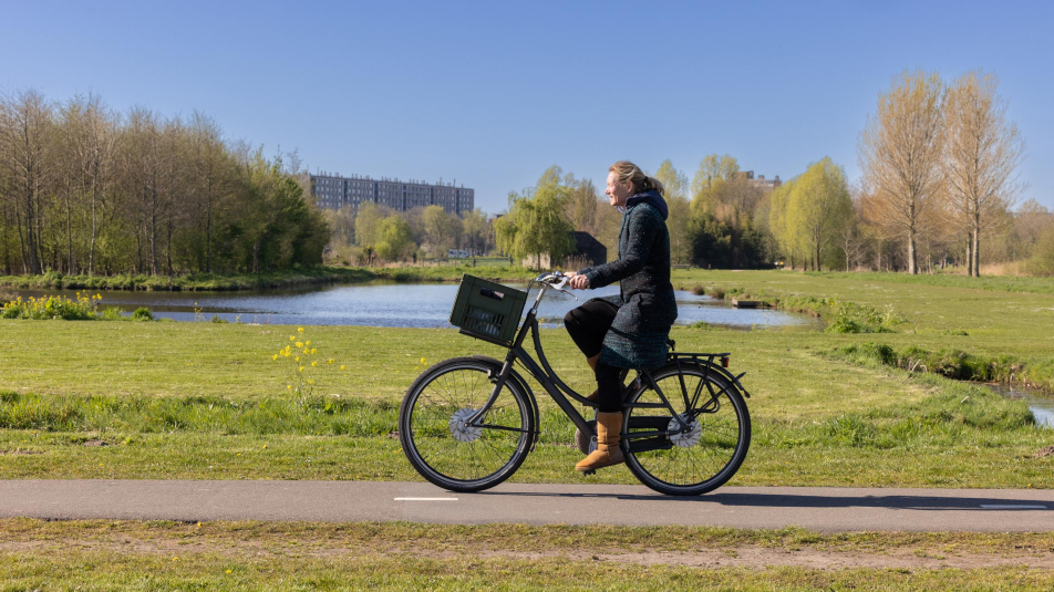 Vrouw fiets door het groen van Noorderpark-Ruigenhoek met flatgebouw op de achtergrond