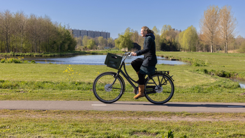 Vrouw fiets door het groen van Noorderpark-Ruigenhoek met flatgebouw op de achtergrond