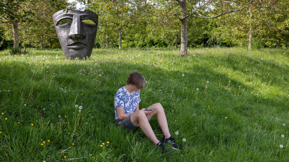 Tiener zit op zijn telefoon in het grasveld van Bos Nieuw Wulven