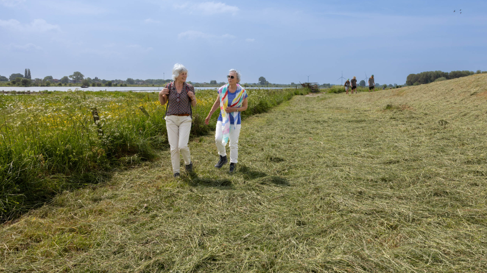 Twee vrouwen wandelen aan de voet van de Lekdijk
